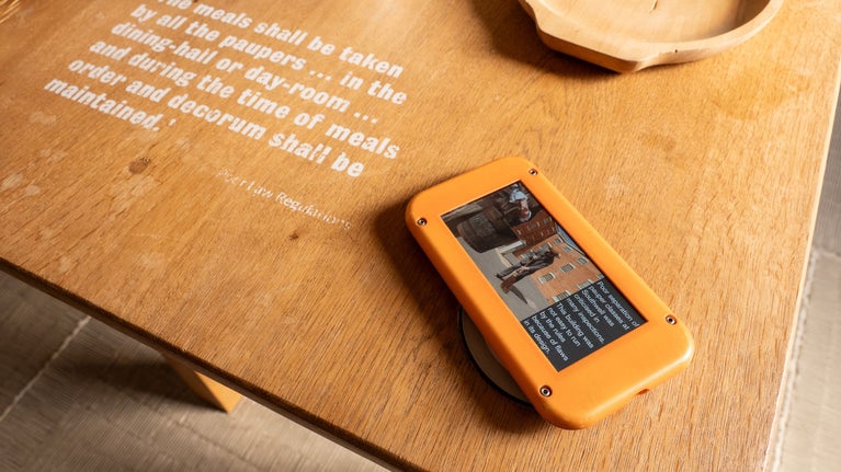 Orange coloured digital device with screen explaining the story of The Workhouse